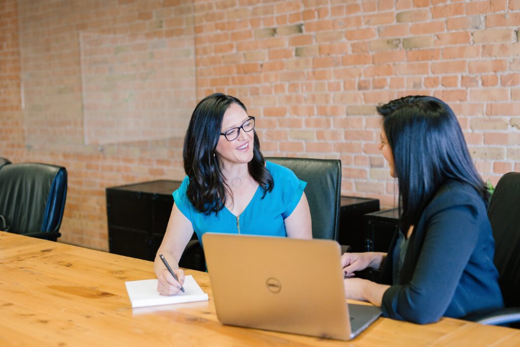 Screenshot of two females at a desk with a laptop