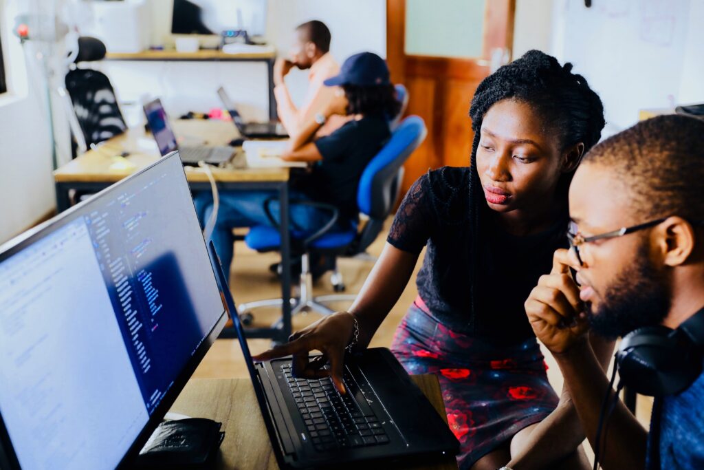 The Coding Assessment Exercise Two people meeting at a desk with a laptop and monitor