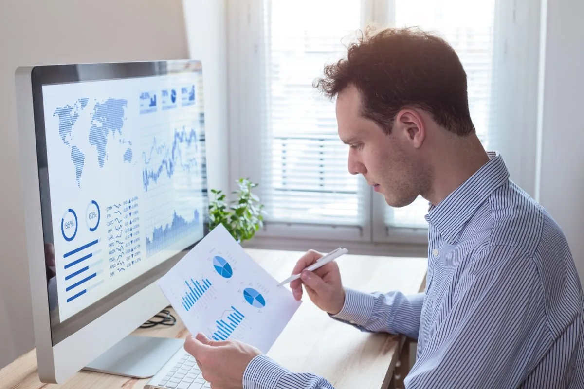 A man looking at charts on paper and on the computer